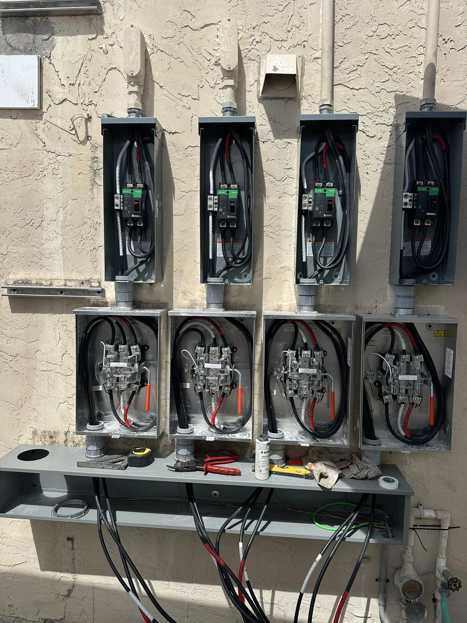 Row of open commercial meter enclosures and main breakers during repair on a stucco wall