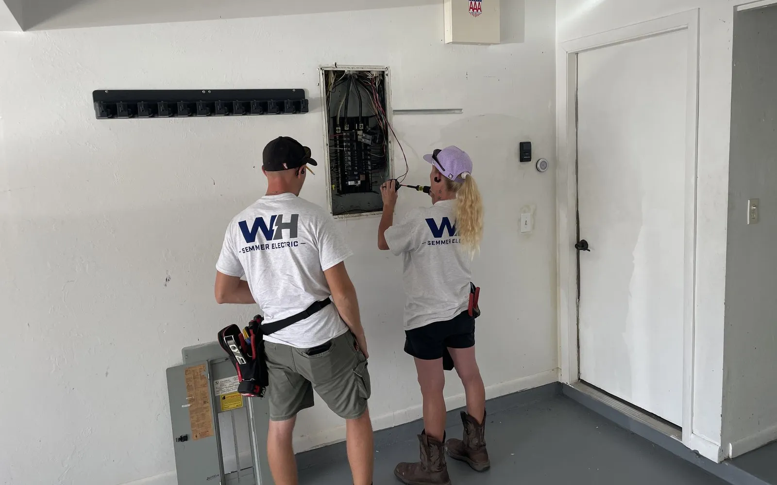 Two WH Semmer Electric crew members working in an open residential electrical panel in a garage