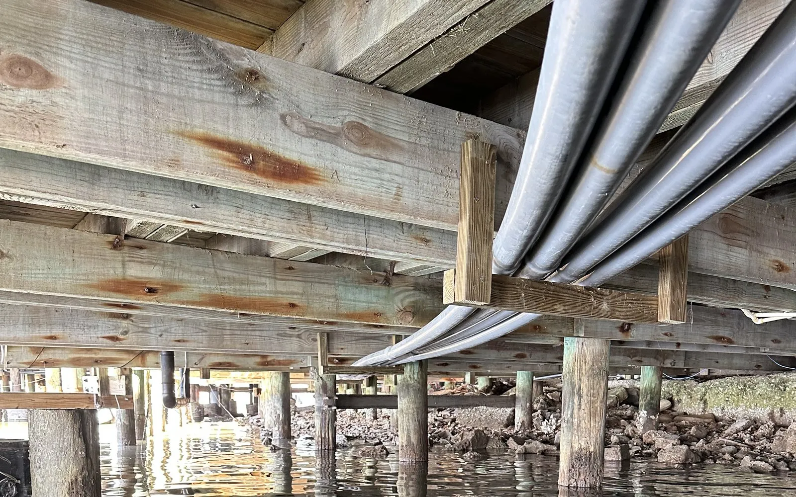 Conduit raceway runs secured to the underside framing of a dock over the water
