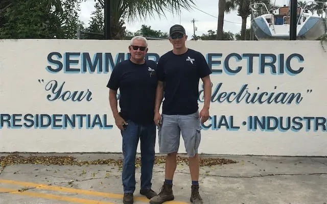 Two generations of Semmer electricians standing in front of the original Semmer Electric sign